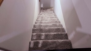 Una escalera alfombrada con paredes blancas y barandilla de madera.