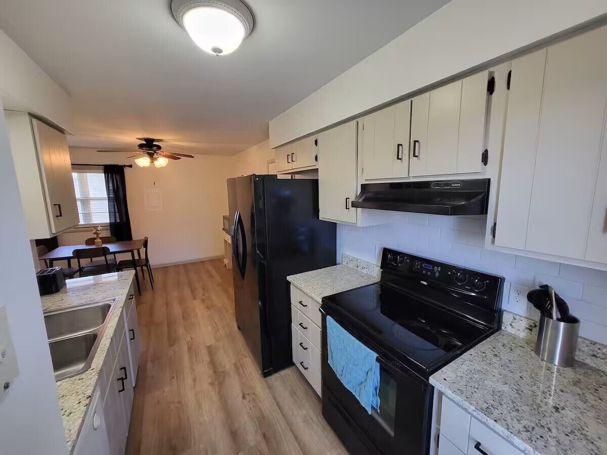 A modern kitchen with white cabinets, a black refrigerator, a stove, and a dining area with a table and chairs.