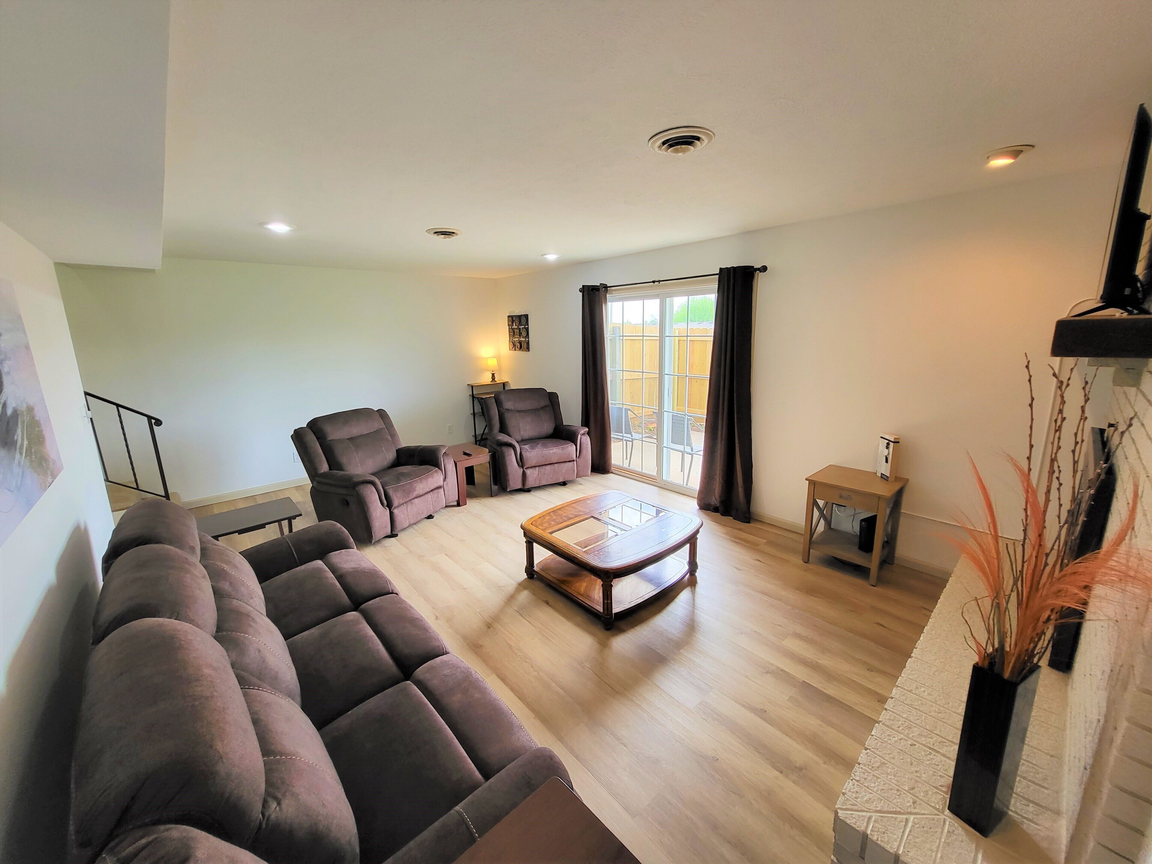 A living room with a sectional sofa, two armchairs, a coffee table, and a sliding glass door leading to a patio.