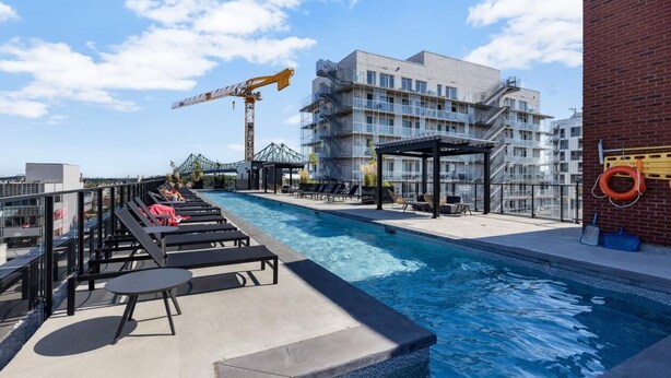Ein Dachpool mit Liegestühlen und einer überdachten Sitzgelegenheit, umgeben von einer Baustelle und einem mehrstöckigen Gebäude.