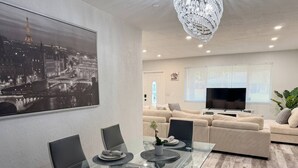 En moderne stue med spisebord i glas, sofa og fjernsyn.