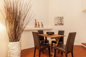 A dining area with a wooden table, four chairs, a vase with branches, and a wall-mounted shelf with decorative items. - Campo dei Fiori Silver Apartment (Roma)