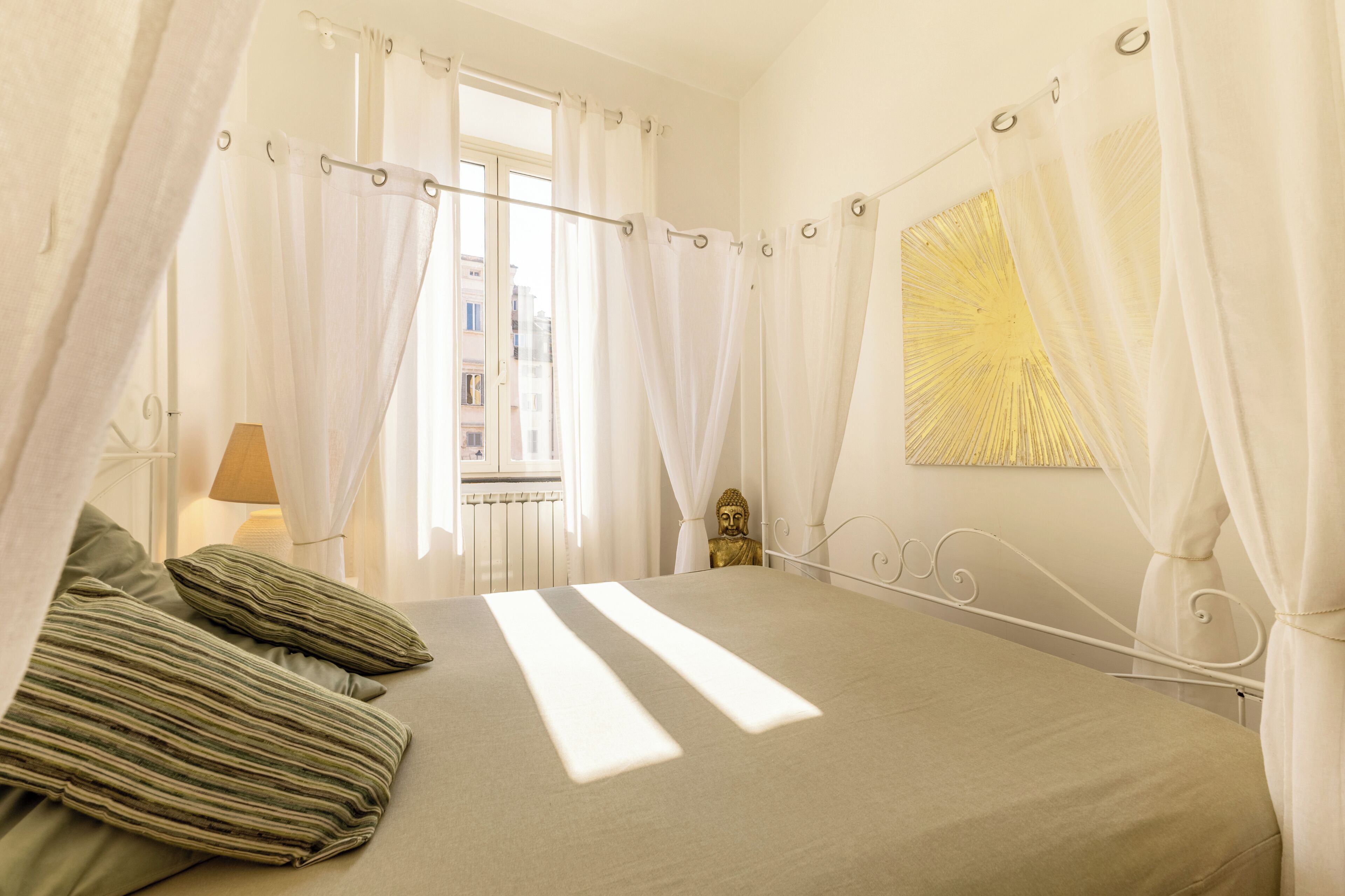 A bedroom with a bed, curtains, a Buddha statue, and a window.
