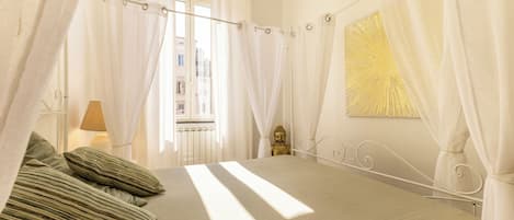 A bedroom with a bed, curtains, a Buddha statue, and a window.