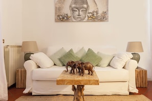A white sofa with green pillows, a wooden coffee table with elephant figurines, and a Buddha painting on the wall. - Campo dei Fiori Silver Apartment (Roma)
