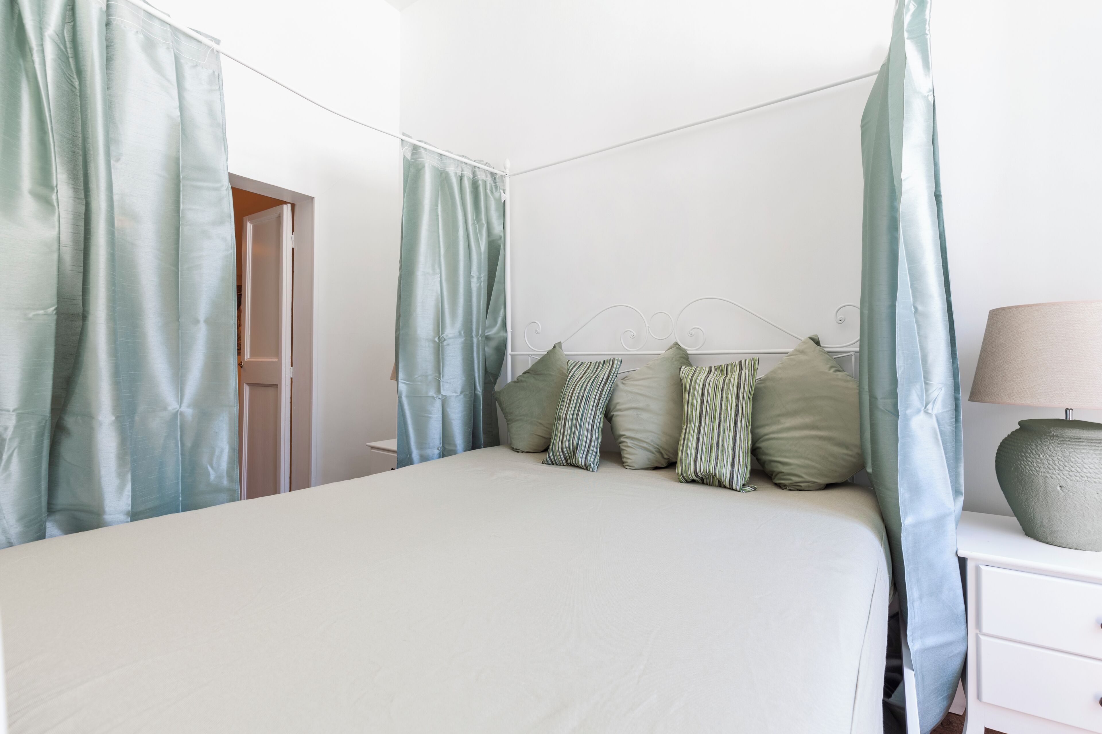 Un dormitorio con cama, cortinas, mesita de noche y lámpara.