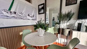 Een eethoek met een ronde tafel, groene stoelen en een witte vaas met planten.