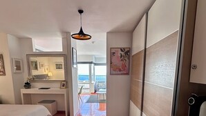 Een hotelkamer met een bed, een bureau, een kledingkast en uitzicht op zee.