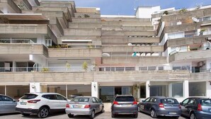 Een meerlaags woongebouw met balkons, een parkeerplaats met meerdere auto's en een heldere lucht.