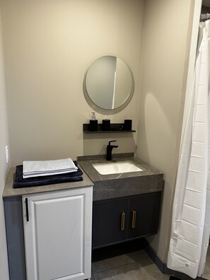Une salle de bain avec un meuble blanc, un lavabo noir, un miroir et un rideau de douche.