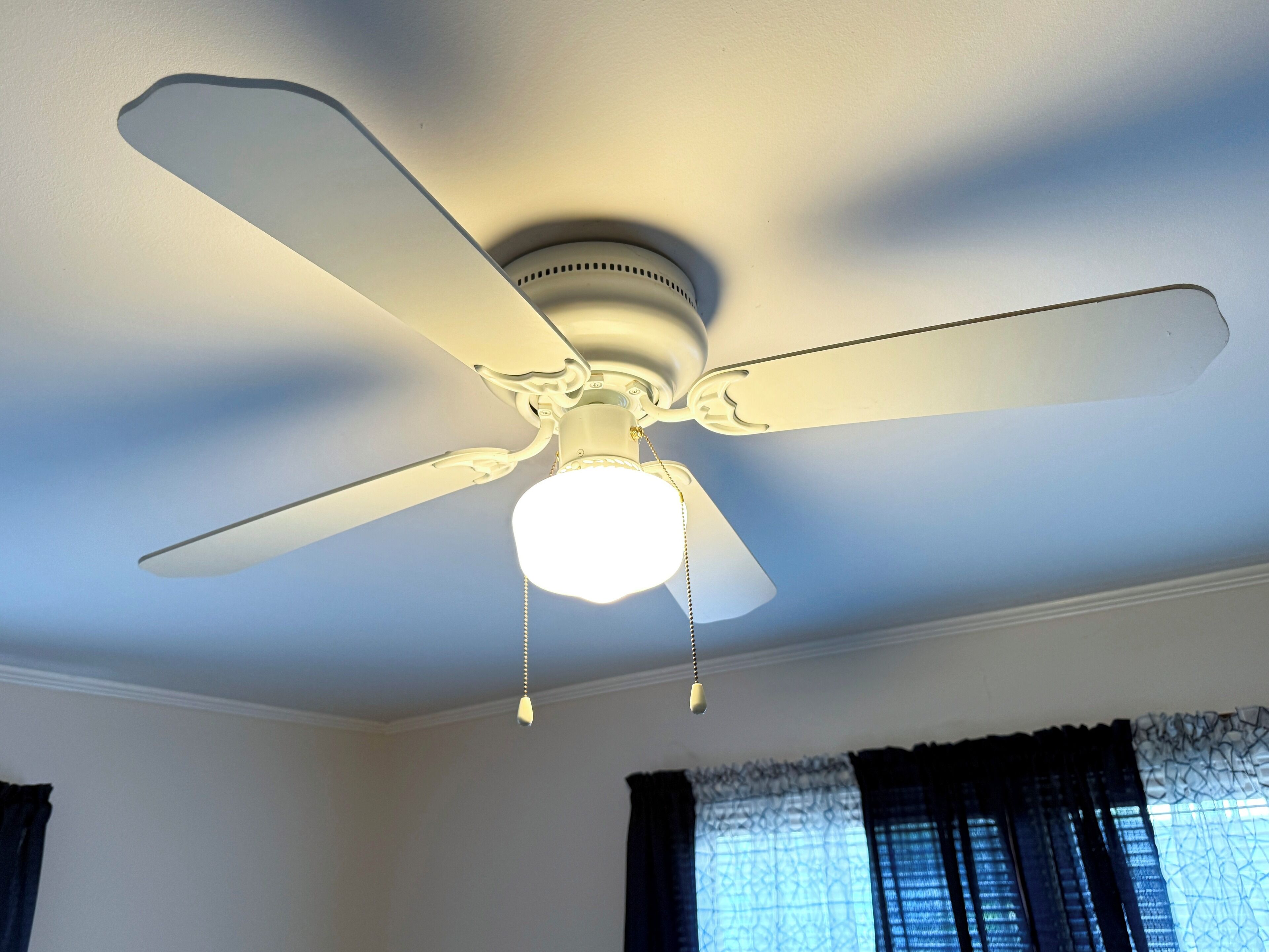 A ceiling fan with a light fixture in a room with dark curtains and a window.