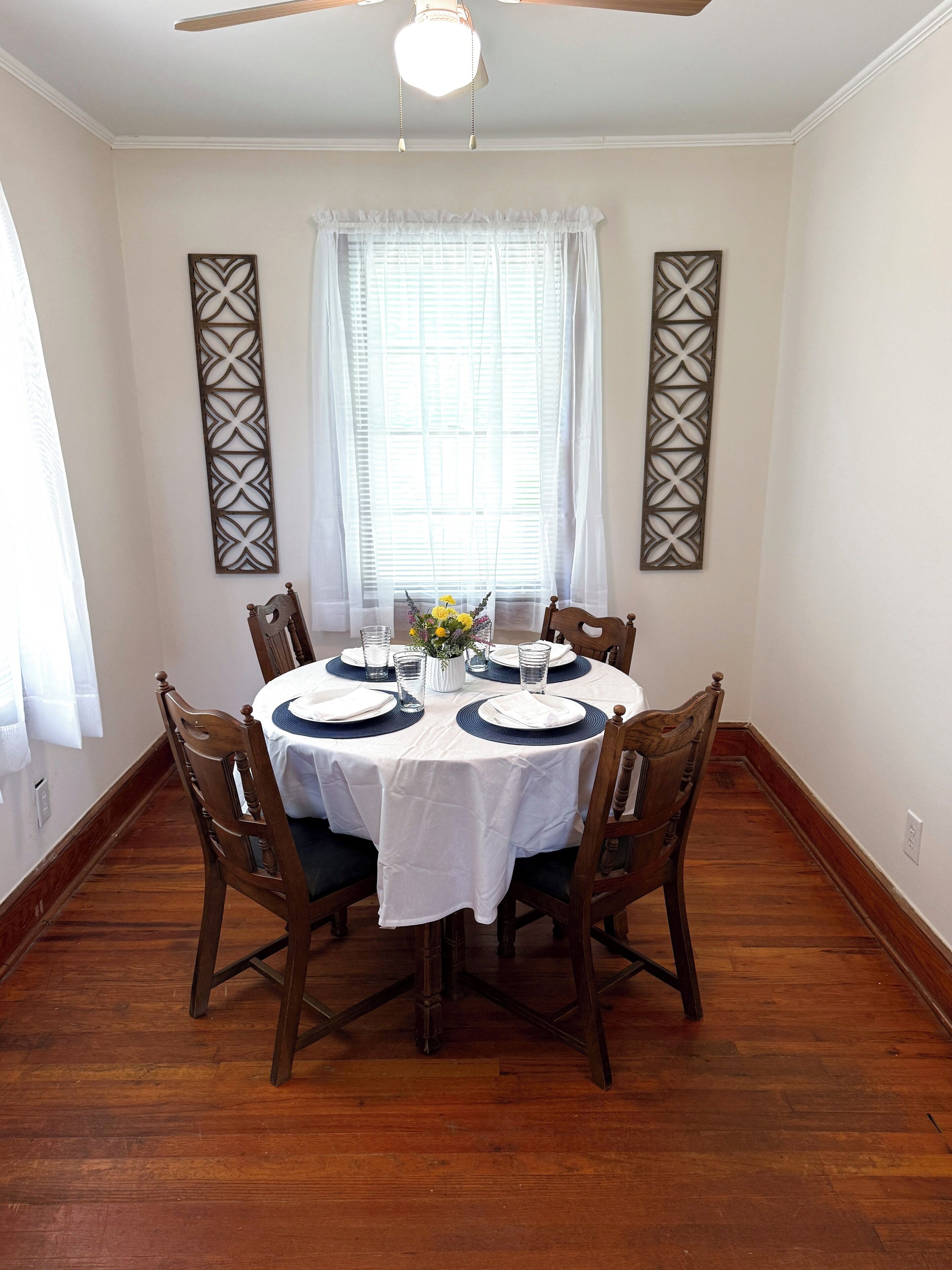 Une salle à manger avec une table ronde dressée pour six personnes, entourée de chaises en bois.