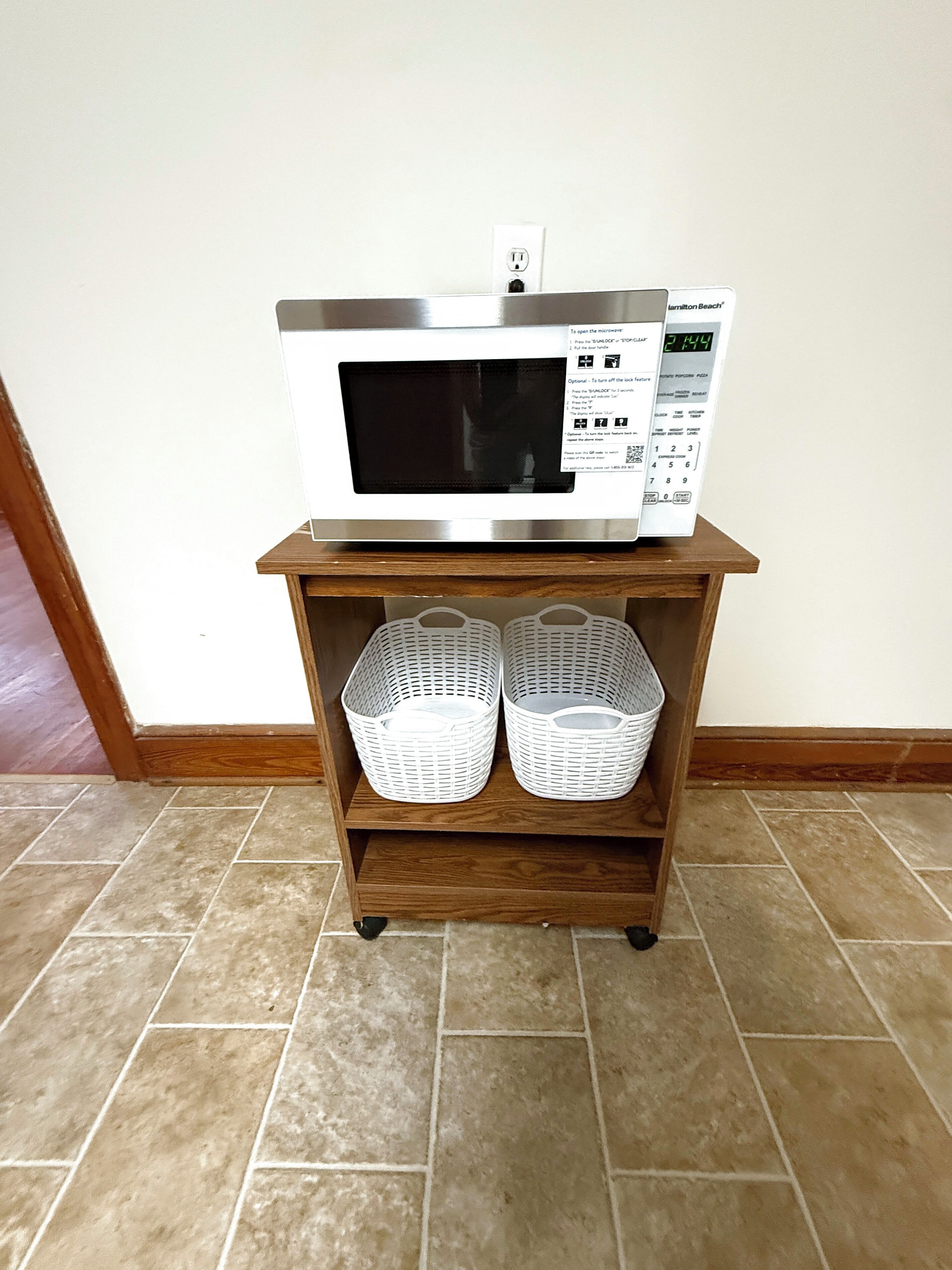 A microwave on a wooden shelf with two white baskets underneath.