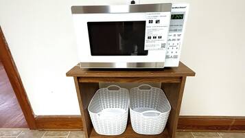 A microwave on a wooden shelf with two white baskets underneath.