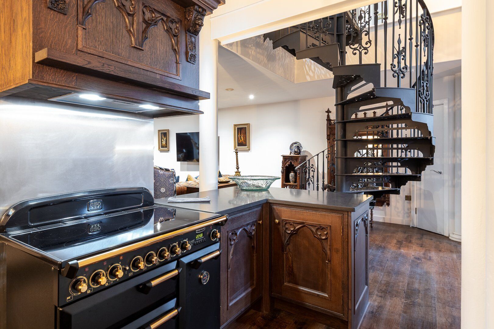 A kitchen with a stove, wooden cabinets, and a staircase with ornate railings.