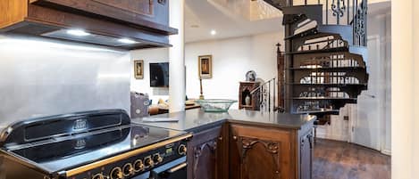 A kitchen with a stove, wooden cabinets, and a staircase with ornate railings.