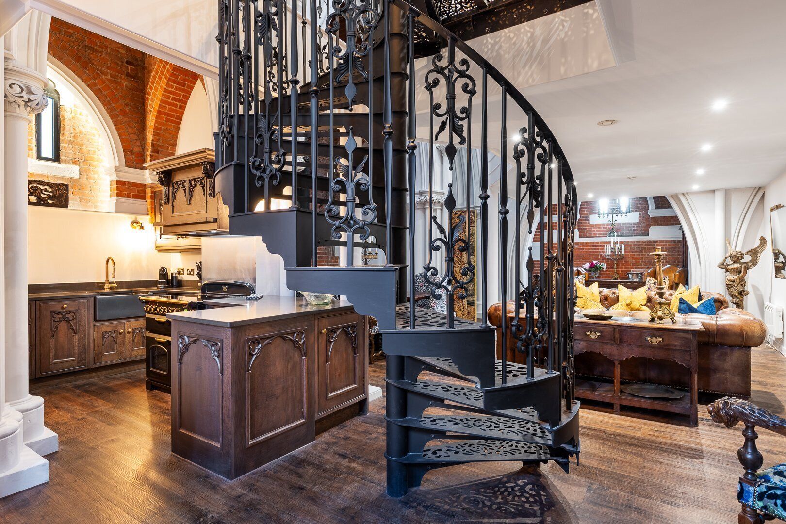 Een ruime keuken met donker houten keukenkastjes, een centraal eiland en een zwart ijzeren spiraaltrap.