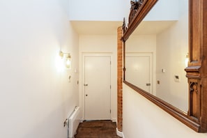 Ein schmaler Flur mit einer Holztreppe, einer weißen Tür und einer Wandleuchte.