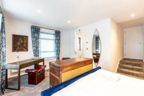 Ein Hotelzimmer mit einem Bett, einem Schreibtisch mit Spiegel, einer Kommode, einem großen Spiegel, einer Tür und einem Fenster mit Vorhängen.