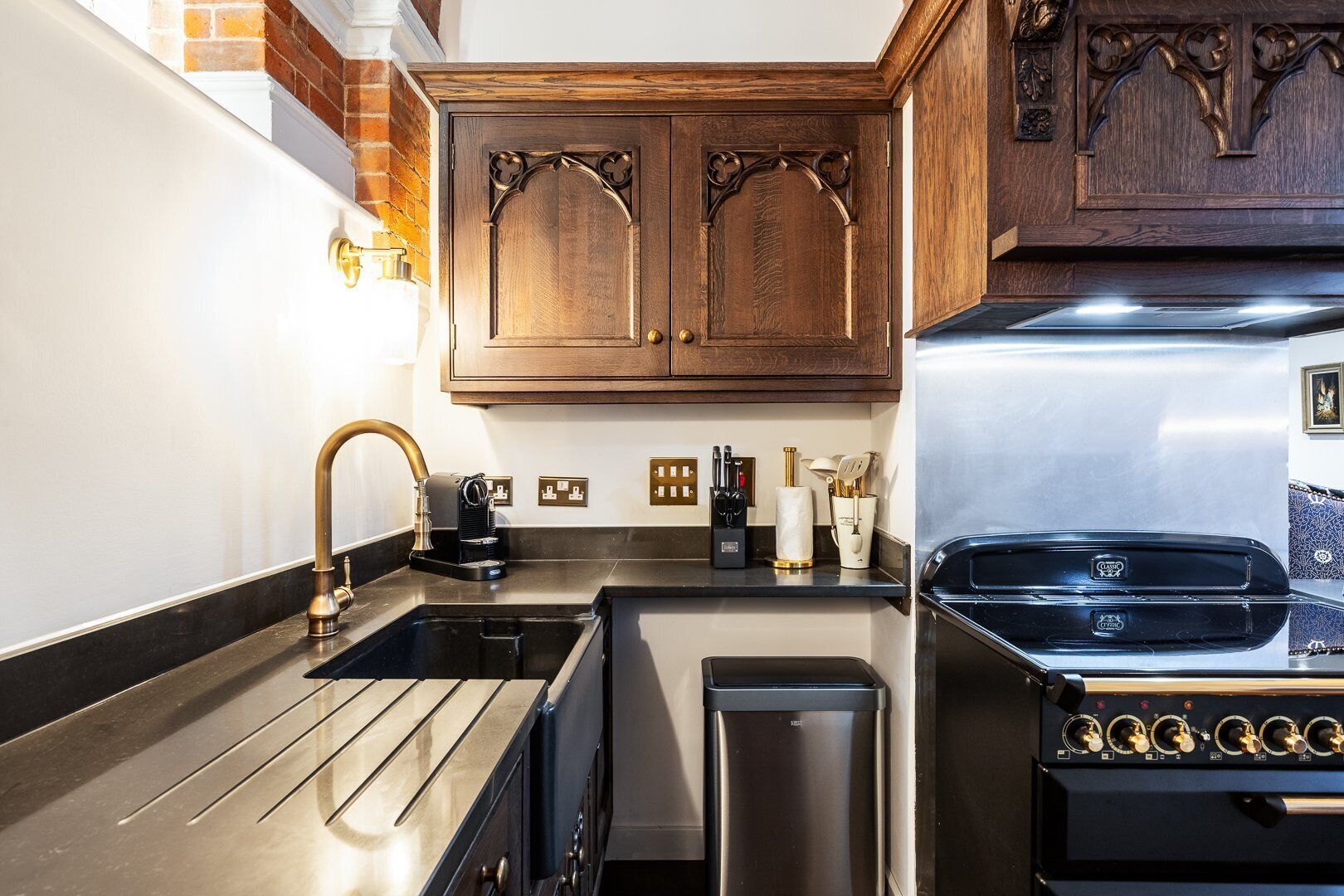 A kitchen with a stainless steel sink, a coffee maker, a trash can, and a stove.