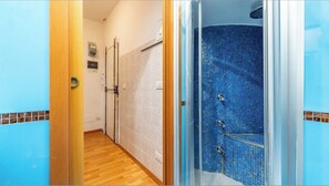 Ein Flur mit Duschbereich, der blaue Mosaikfliesen, Holzboden und eine Tür mit Metallgriff aufweist.