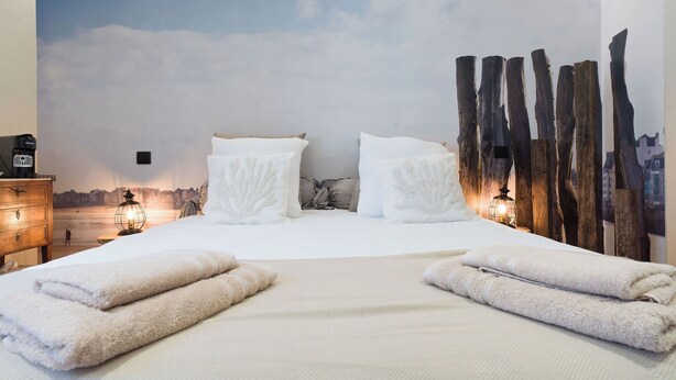 A hotel room with a bed, two pillows, a nightstand with a lamp, and a wall mural. - Les Grèves, Village Center, 80 meters from the beach (Saint-Jacut-de-la-Mer)