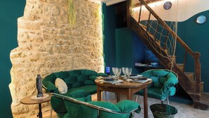 A room with a stone wall, a green sofa, a wooden table, and a staircase. - Les Grèves, Village Center, 80 meters from the beach (Saint-Jacut-de-la-Mer)
