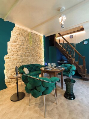 A room with a stone wall, a green sofa, a wooden table, and a staircase. - Les Grèves, Village Center, 80 meters from the beach (Saint-Jacut-de-la-Mer)