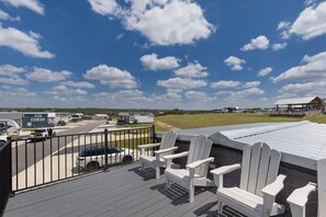 Eine Terrasse mit weißen Adirondack-Stühlen, Blick auf einen Parkplatz und einen klaren Himmel.