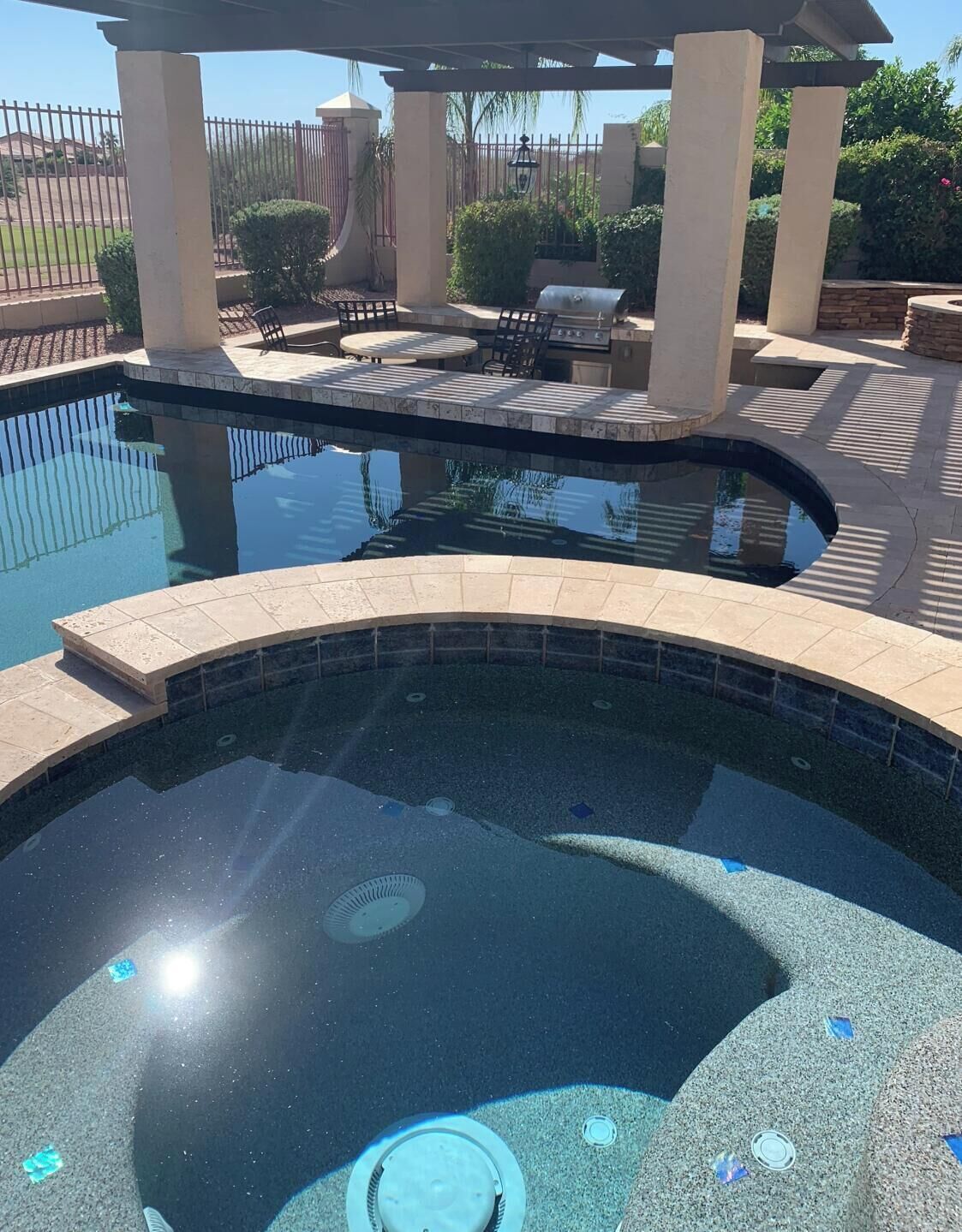 A swimming pool with a sunken center, surrounded by a patio area with chairs and a grill.