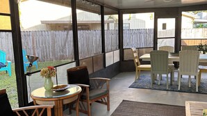 Un patio coperto con tavolo e sedie, una grande finestra e vista su una recinzione in legno.