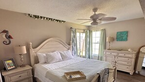 Una camera da letto con un letto, comodini, una cassettiera, una ventola a soffitto e una finestra con tende.