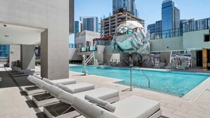Ein Pool auf dem Dach mit Liegestühlen, einem Sprungbrett und einer großen, modernen Skulptur.