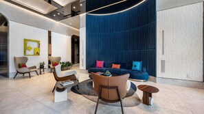 Um lobby moderno com uma parede azul curva, área de estar com sofás e poltronas, e uma mesa de centro.