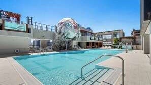A swimming pool with a modern architectural feature, a poolside area with lounge chairs, and a clear sky. - E2611 - West-View Studio with Balcony in Downtown Miami (Miami)