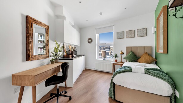 A bedroom with a bed, desk, chair, and a view of the city through a window. - Cozy and Lovely Studio - Close to everything! (London)
