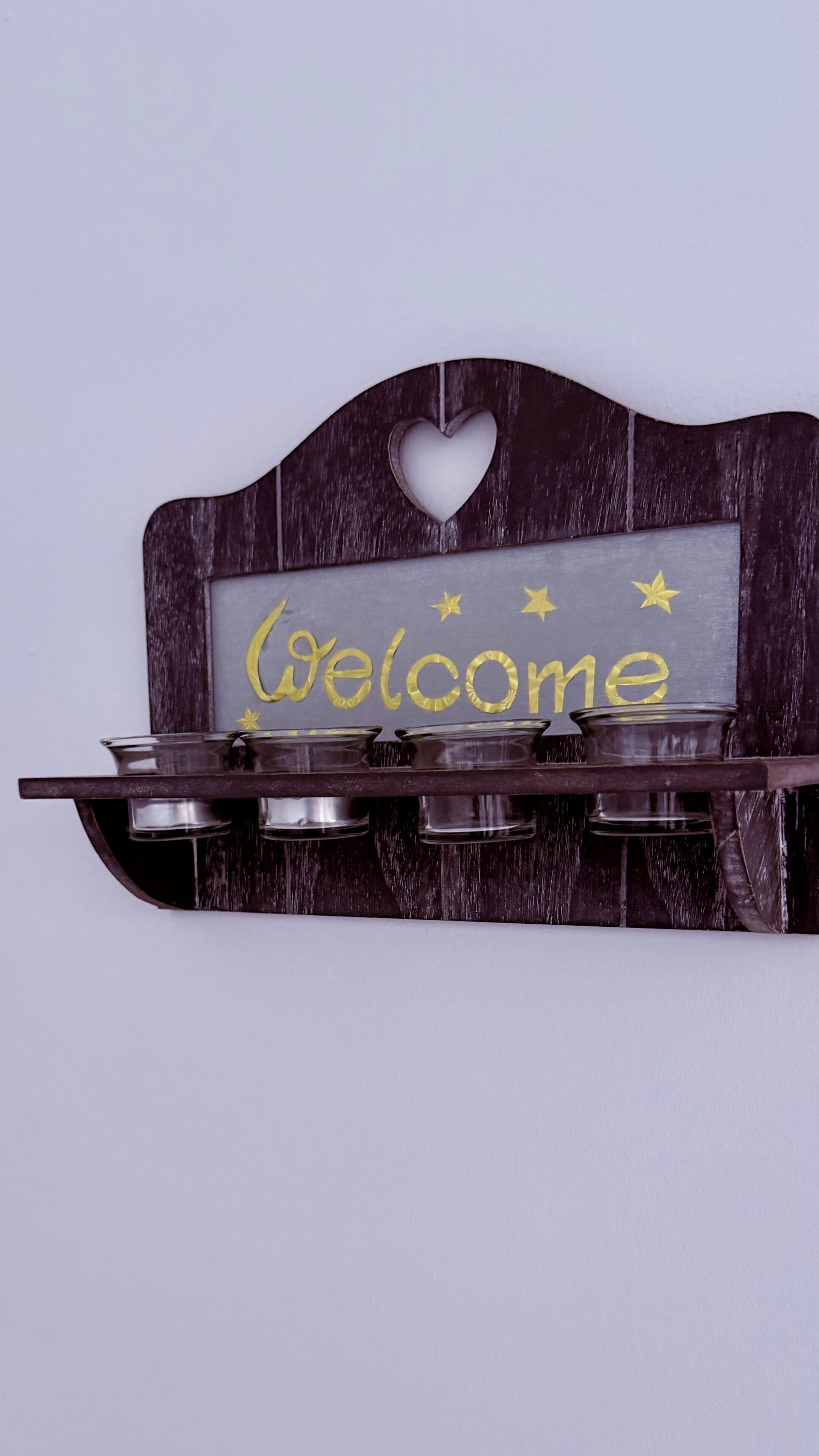 Un letrero colgado en la pared con la palabra 'Welcome' y estrellas decorativas, montado sobre una estructura de madera con un corte en forma de corazón.