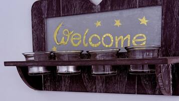 Un letrero colgado en la pared con la palabra 'Welcome' y estrellas decorativas, montado sobre una estructura de madera con un corte en forma de corazón.