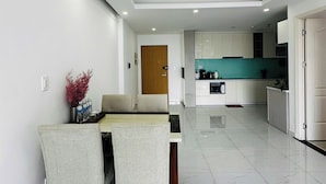 A modern kitchen with white cabinets, a teal backsplash, and a dining area with a marble table and chairs. - Diamond Luxury (Ho Chi Minh City)