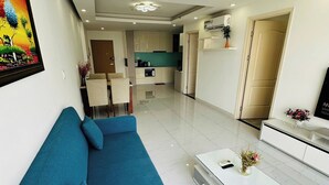 A modern living room with a blue sofa, a white coffee table, and a kitchen in the background. - Diamond Luxury (Ho Chi Minh City)