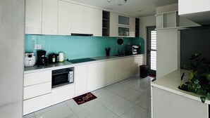 A modern kitchen with white cabinets, a teal backsplash, and a microwave. - Diamond Luxury (Ho Chi Minh City)