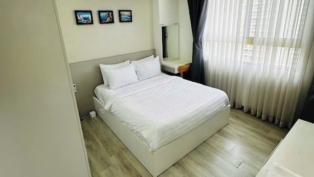 A hotel room with a bed, a bedside table, a mirror, and a window with curtains. - Diamond Luxury (Ho Chi Minh City)