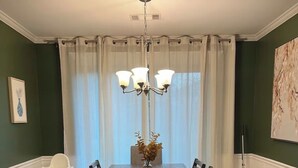 En spisestue med et bord, stole, en lysekrone, en bordløber og en stol med bakke.