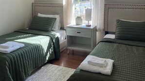 Et soveværelse med to senge, et skrivebord, et vindue med gardiner og en loftsvifte.
