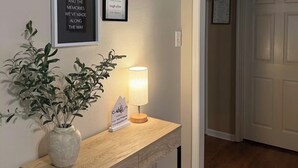 En gang med en velkomstskilt, et indrammet citat, en potteplante og et skrivebord med en lampe.