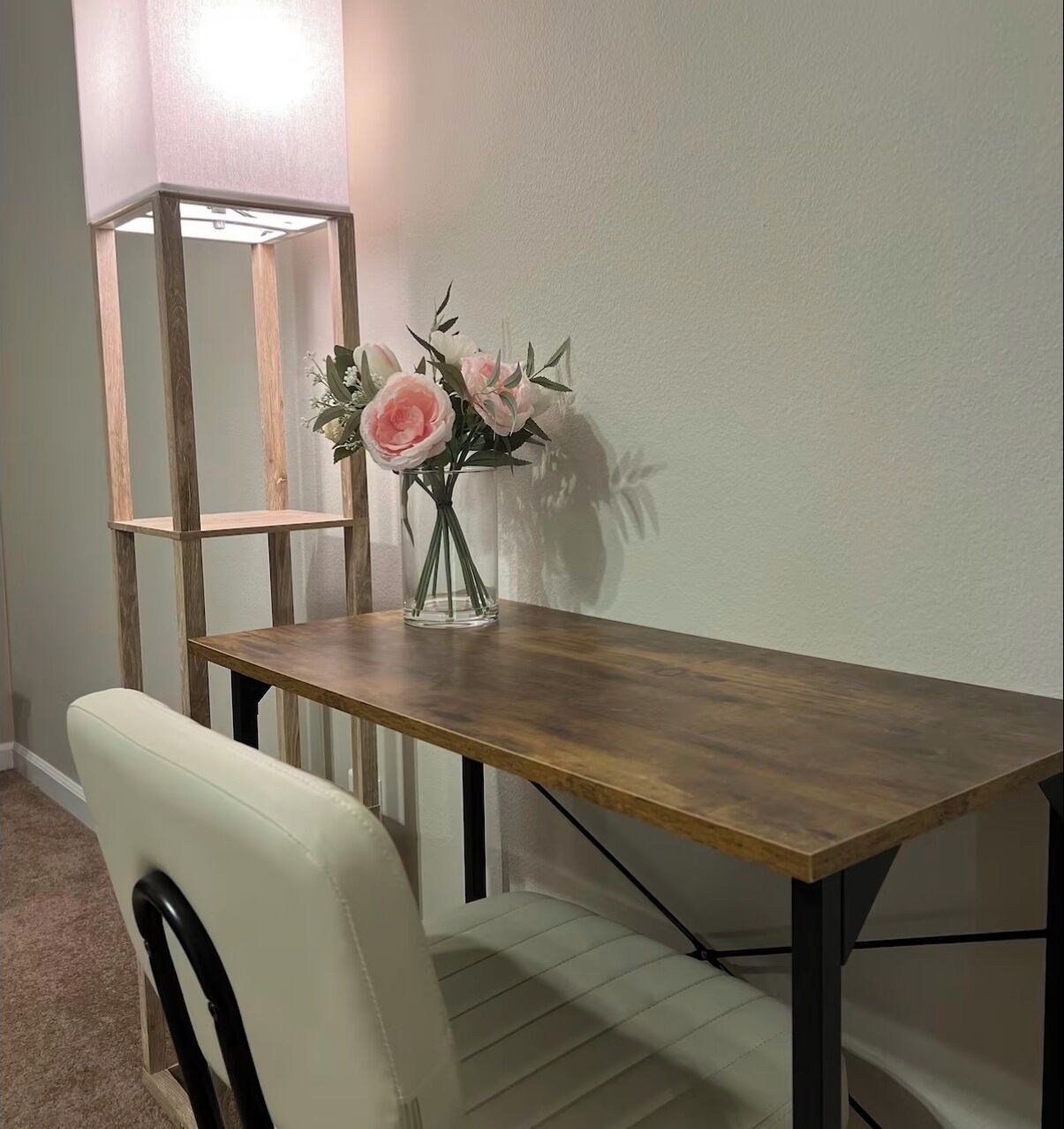 A dining table with a vase of flowers, a chair, and a tall, narrow shelf unit against a plain wall.