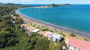An aerial view of a coastal area with a beach, boats, and buildings. - Beachfront Penthouse with Panoramic Ocean Views (Playa Potrero)
