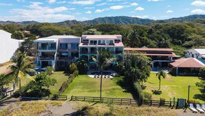 A multi-story building with balconies, surrounded by lush greenery and a mountainous backdrop. - Beachfront Penthouse with Panoramic Ocean Views (Playa Potrero)