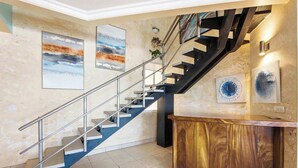 A modern interior with a staircase, artwork, and a wooden reception desk. - Beachfront Penthouse with Panoramic Ocean Views (Playa Potrero)