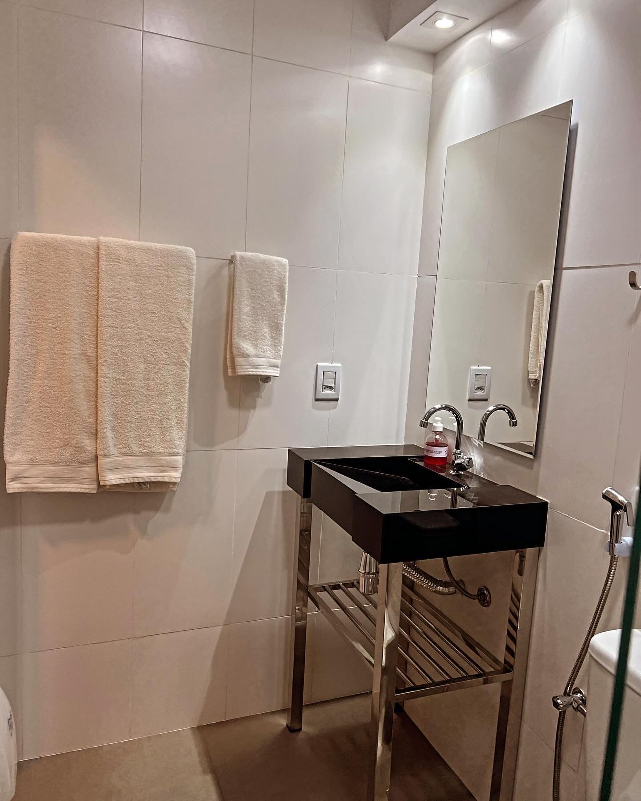Un baño con lavamanos, espejo, toallero y ducha.